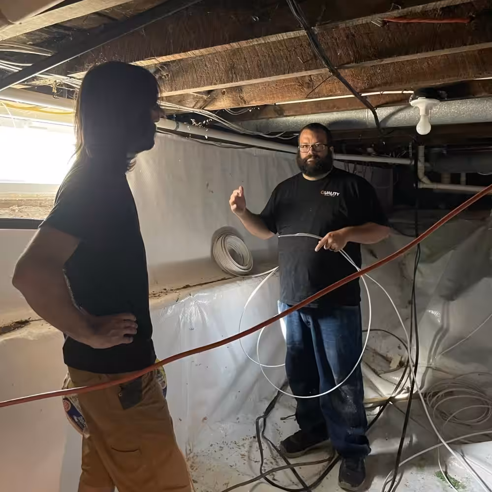 Crawl space electrical rough-in with technician holding cable during renovation.
