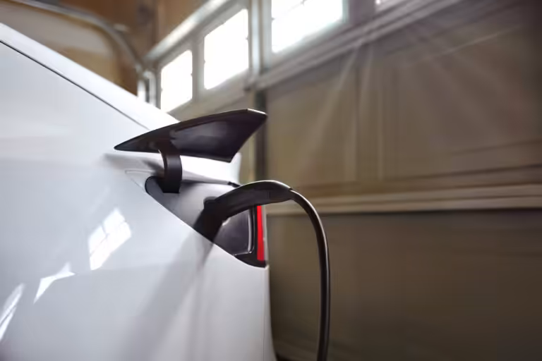 White electric vehicle charging with a Level 2 charger plugged into its port inside a sunlit New Hampshire garage, showcasing a home EV charging setup.