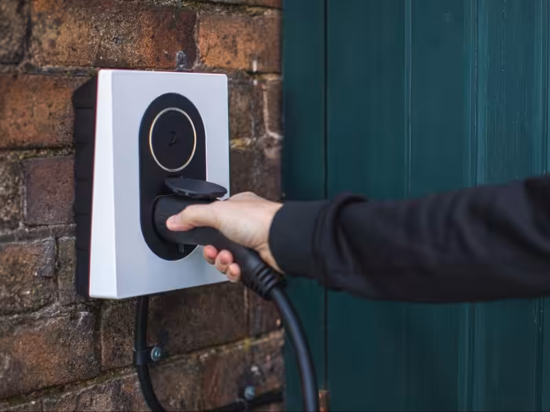 Person plugging in an electric vehicle charger mounted on a brick wall after home EV charger installation